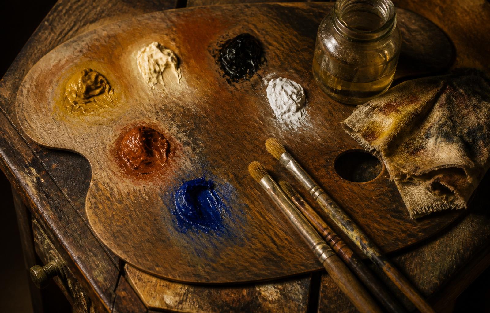 An oil painter's taboret with a limited palette laid out in warm ochre, black, white, burnt sienna, and ultramarine blue.